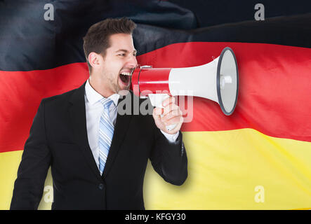 Portrait of young businessman shouting par mégaphone en face de drapeau allemand Banque D'Images