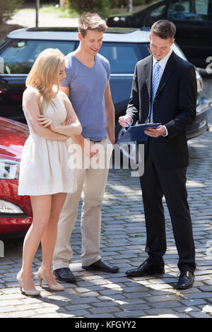 Young salesman montrant le papier du contrat de couple par nouvelle voiture Banque D'Images