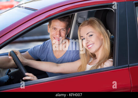 Portrait of happy young woman with man sitting in new car Banque D'Images