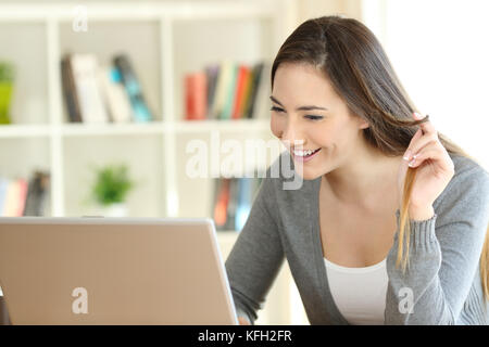 Fille candide datant en ligne avec un ordinateur portable et de toucher à la maison de cheveux Banque D'Images