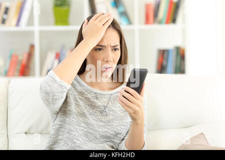 Portrait d'une femme inquiète faire erreur sur un téléphone intelligent assis sur un canapé à la maison Banque D'Images