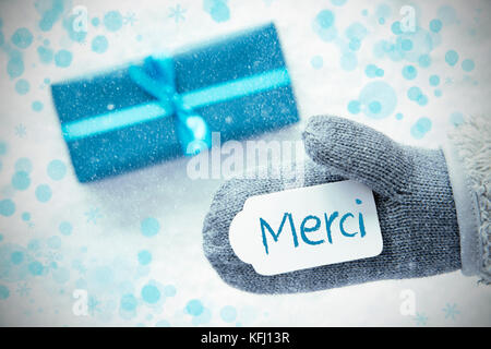 Gant avec étiquette avec texte français merci veut dire merci. turquoise cadeau ou présent sur neige en arrière-plan. avec des flocons de cartes de vœux et b Banque D'Images