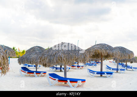 Des chaises longues sous un parasol sur la plage de sable Banque D'Images