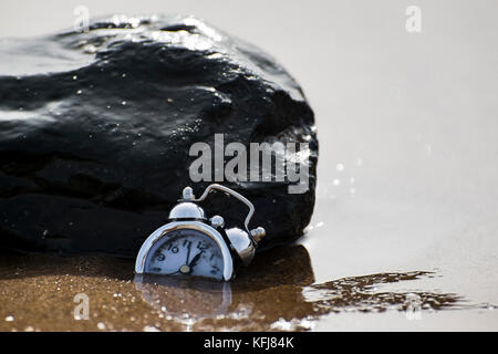 Un abrégé consept tiré d'un réveil s'enfoncer dans le sable entouré par les courants d'eau de mer ce qui signifie le passage du temps Banque D'Images