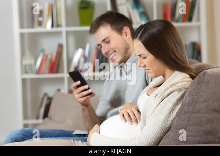 Mari à l'aide d'un téléphone intelligent est ignorant sa femme enceinte souffrant maux de ventre assis sur un canapé à la maison Banque D'Images