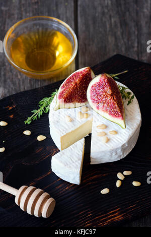 Le camembert avec des figues fraîches, le miel et les noix de pin sur la planche à découper en bois sombre. Vue rapprochée Banque D'Images