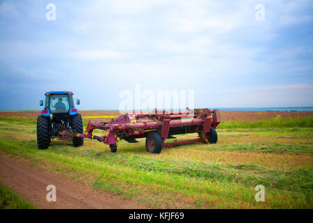 Le tracteur avec la faucheuse dans le domaine de la luzerne et du sainfoin Banque D'Images