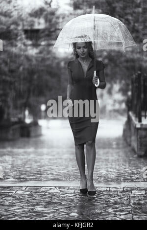License and prints at MaximImages.com - Jeune femme dans une robe rouge élégante avec un parapluie marchant sur un jour de pluie sur une ville pavée Banque D'Images