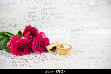 Noël Nourriture photographie image avec xmas glitter roses rouges et petits pâtés glacé brillant blanc sur fond de papier d'emballage avec l'écriture de fête Banque D'Images