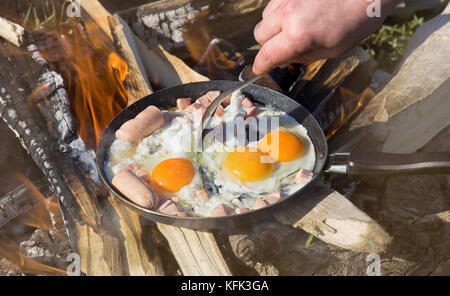 Le petit-déjeuner sur la nature d'un pique-nique. œufs brouillés frits sur charbons dans une casserole en feu Banque D'Images