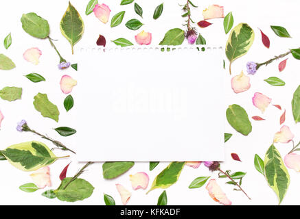 Une feuille de papier du texte dans un cadre de fleurs, de pétales et de feuilles vertes sur fond blanc.droit d'inspiration.type télévision, vue du dessus Banque D'Images