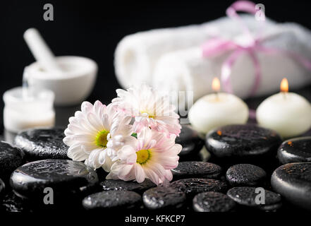 Arrière-plan de spa fleurs Daisy, bougies, crème cosmétique, les serviettes blanches et pierres de basalte zen avec de l'eau tombe sur noir Banque D'Images