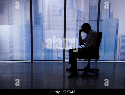 Vue de côté toute la longueur tendue businessman sitting on chair par fenêtre de bureau Banque D'Images