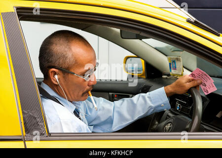 Un chauffeur de taxi thaïlandais fume et prend un moment dans la circulation pour vérifier son téléphone. Banque D'Images