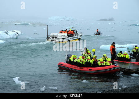 Touristes en bateaux zodiac quittant la rive Jokulsarlon lagon glaciaire tour, hivernage journée observation icebergs portant des gilets de sauvetage jaune vif sud de l'Islande Banque D'Images