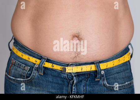 Portrait de gros plan homme avec bande mesure autour de taille contre l'arrière-plan gris Banque D'Images