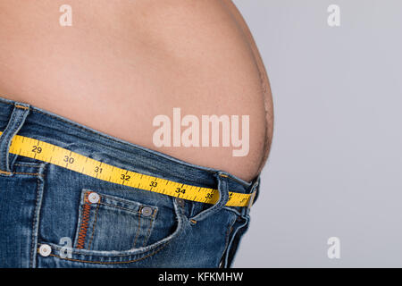 Vue de côté au milieu du gros homme avec bande mesure autour de taille contre l'arrière-plan gris Banque D'Images