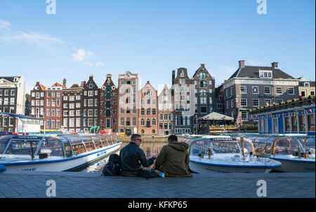 Amsterdam, Pays-Bas - le 19 août 2017 ; deux hommes assis sur le côté ombragé du canal dans l'architecture de façades d'une gamme de modèles pour lesquels la ville Banque D'Images