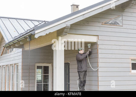 L'électricien installe l'éclairage extérieur, un feu déclenché par la motion sur le mur d'une maison à ossature en bois magnifique, Banque D'Images