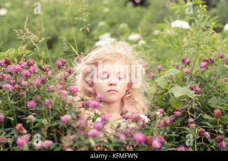 Petite fille blonde avec des fleurs de trèfle rose autour dans le pré Banque D'Images