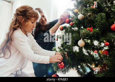 Mère et fille de l'arbre de Noël de décoration à la maison. Petite fille aider sa mère dans la décoration de sapin de Noël. Banque D'Images