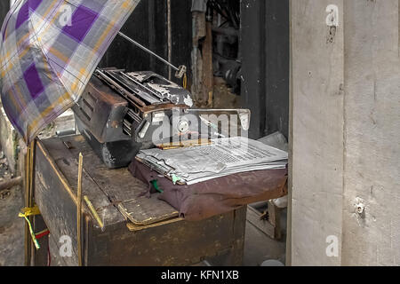 VINTAGE TYPEWRITER. Rusty et vieille machine à écrire avec une pile de documents sont sur une table en bois. Un parapluie liée à une table pour donner de l'ombre. Banque D'Images