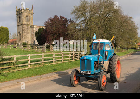 Homme conduisant les old blue vintage tracteur au travers de village Bugthorpe sur Wolds Vintage Group Cours sur la route, un événement annuel de bienfaisance - Yorkshire, Angleterre, Royaume-Uni. Banque D'Images