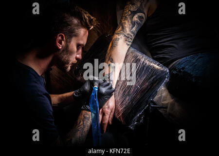 Le barbu tatoueur fait un tatouage sur la main d'un homme Banque D'Images