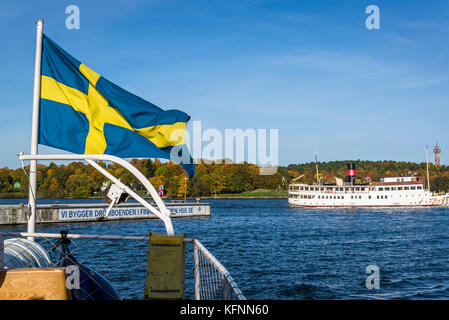 Drapeau suédois sur un bateau et l'île de Djurgarden en arrière-plan, Stockholm, Suède Banque D'Images