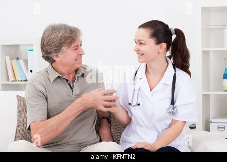 Jeune médecin donne verre d'eau pour le patient d'âge mûr Banque D'Images