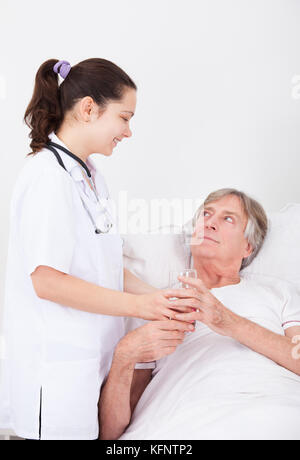 Young female doctor giving verre d'eau pour senior patient Banque D'Images