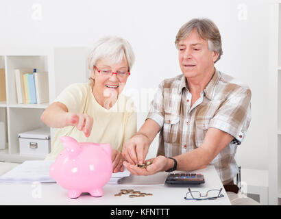 Portrait of smiling senior couple calcul de pièces dans la tirelire rose Banque D'Images
