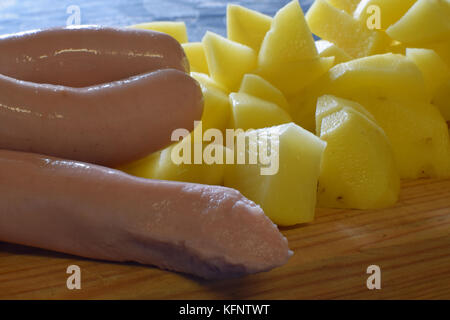 Saucisses fraîches et pommes de terre en tranches sur une planche à découper. Banque D'Images