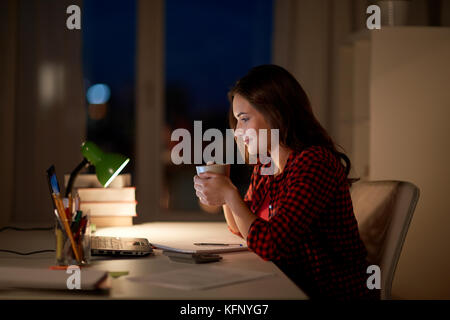 Femme étudiant avec ordinateur portable et café à la maison de nuit Banque D'Images