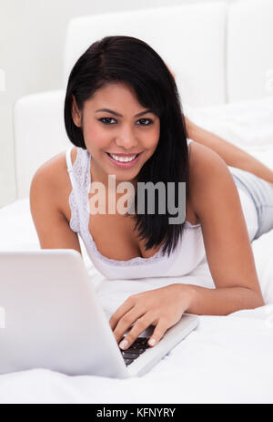 Portrait of young woman lying on bed and using a laptop Banque D'Images