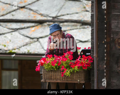 Herbriggen, Suisse - vieil homme fume sur balcon près de boite à fleurs. Banque D'Images