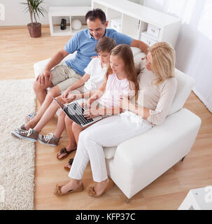 Une famille heureuse avec deux enfants assis sur un canapé à l'aide d'ordinateur portable à la maison Banque D'Images