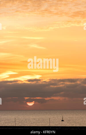 Lever de soleil sur la Manche. Soleil au-dessus de l'horizon en partie caché par la couche de nuage. Ciel Orange. Vu de Ramsgate, dans le Kent. Banque D'Images