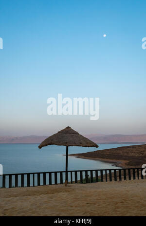 Tôt le matin, avec la lune dans le ciel à Holiday Inn Dead Sea Resort, pas de gens sur la plage et parapluie de paille, Jordanie, Moyen-Orient Banque D'Images