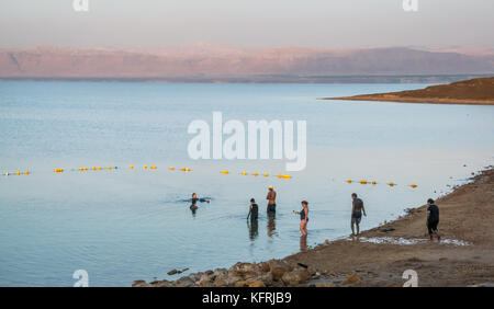Tôt le matin, l'établissement Holiday Inn Dead Sea beach resort, avec des gens couverts de boue et flottant dans l'eau salée, et vue de Cisjordanie, Jordanie, Moyen-Orient Banque D'Images