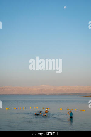 Tôt le matin, l'établissement Holiday Inn Dead Sea beach resort, en Jordanie, avec des gens qui flottent dans l'eau salée et de prendre des photos, avec la lune dans le ciel Banque D'Images