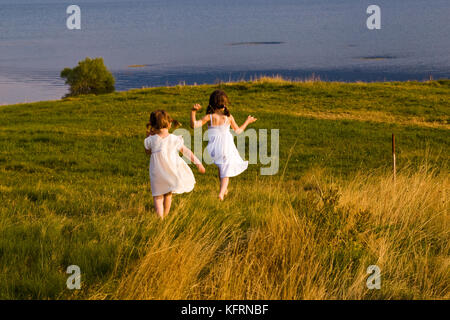 Deux jeunes filles courant dans la prairie d'été, robes blanches. Une émotion heureuse Banque D'Images