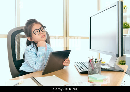 Young cute little girl déguisée en business mobile worker holding digital tablet sitting in office rêverie et une sensation de fatigue. Banque D'Images