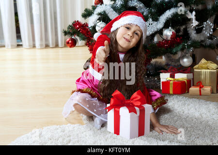 Célébration de Noël, vacances d'hiver et les gens concept. Jeune fille heureuse avec des cadeaux dans les cases assis près d'un arbre de Noël décoré à la maison Banque D'Images