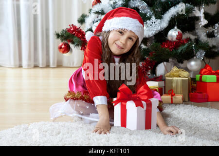 Célébration de Noël, vacances d'hiver et les gens concept. Jeune fille heureuse avec des cadeaux dans les cases assis près d'un arbre de Noël décoré à la maison Banque D'Images