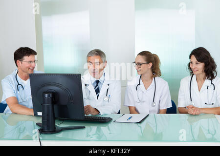 Les médecins ayant une réunion assis à une table en face d'un ordinateur à discuter des études de cas Banque D'Images