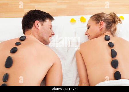 Couple un massage aux pierres chaudes dans un spa où des pierres chauffées sont placées le long de la colonne vertébrale pour détendre les muscles Banque D'Images