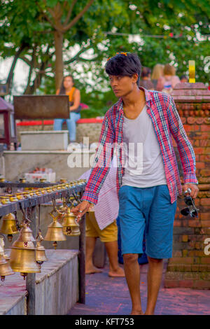 Pokhara, Népal, 10 octobre 2017 : Jeune homme touchant les cloches de tailles différentes en barahi taal mandir, Pokhara, Népal Banque D'Images