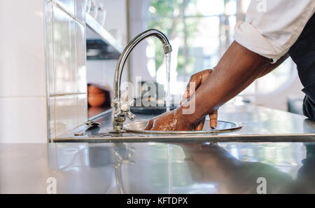 Close up of chef de laver ses mains en cuisine commerciale. L'homme se laver les mains dans un lavabo avec l'eau du robinet. Banque D'Images