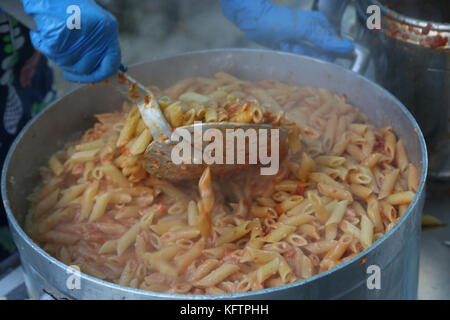 Pot géant avec des pâtes avec sauce tomate rouge et bleu des gants pendant la livraison de repas Banque D'Images